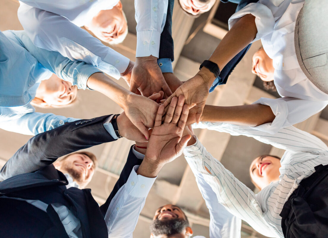 United Colleagues Standing In Circle Holding Hands In Office, Bottom View